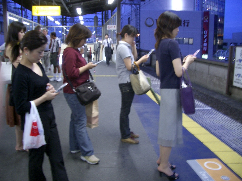 5 Japanese women browsing the web on their phones while waiting for a train