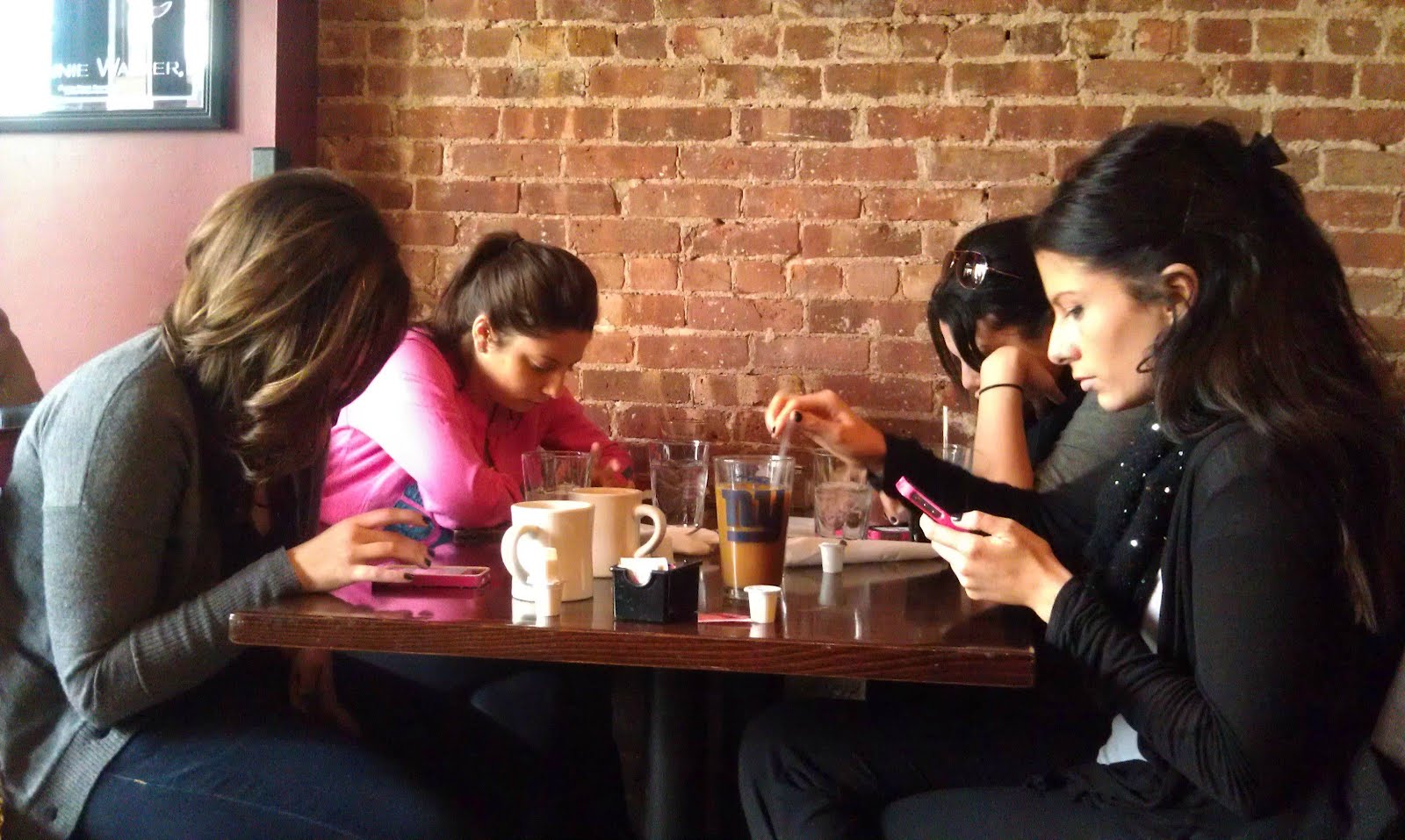 Four teenagers sitting in a cafe and each fully immersed in her mobile phone