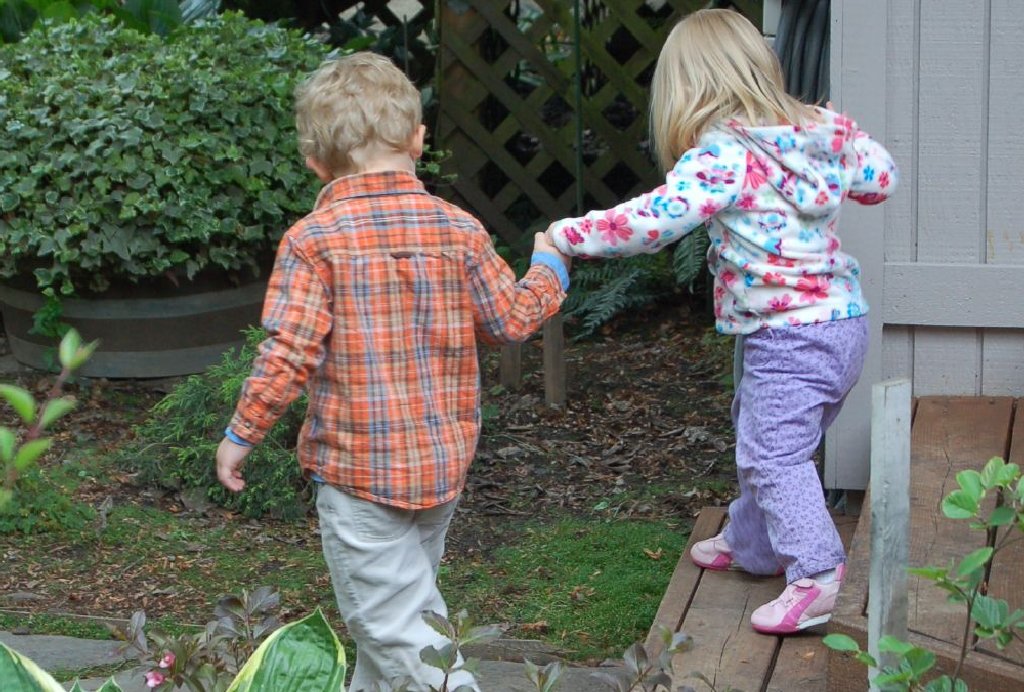 A young boy helps a young girl down the steps by holding her hand