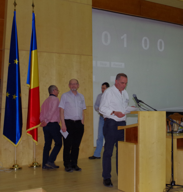 one person standing at the podium, 3 more lined up behind ready to speak. A large timer shows 1 minute on the wall behind them