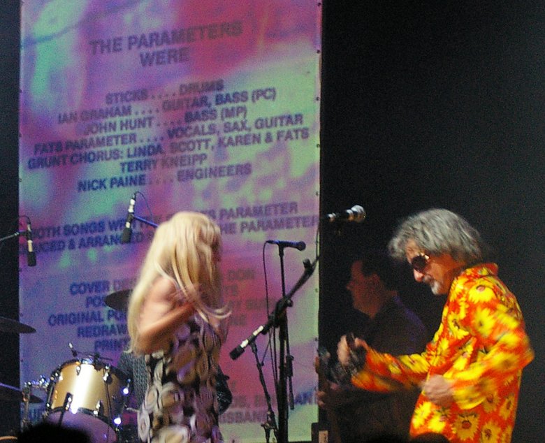 Three musicians on stage. Behind them the backdrop credits the members of hte band which is called 'The Parameters'