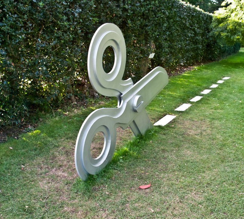 A sculpture of a large pair of scissors cutting along a dotted line in the grass