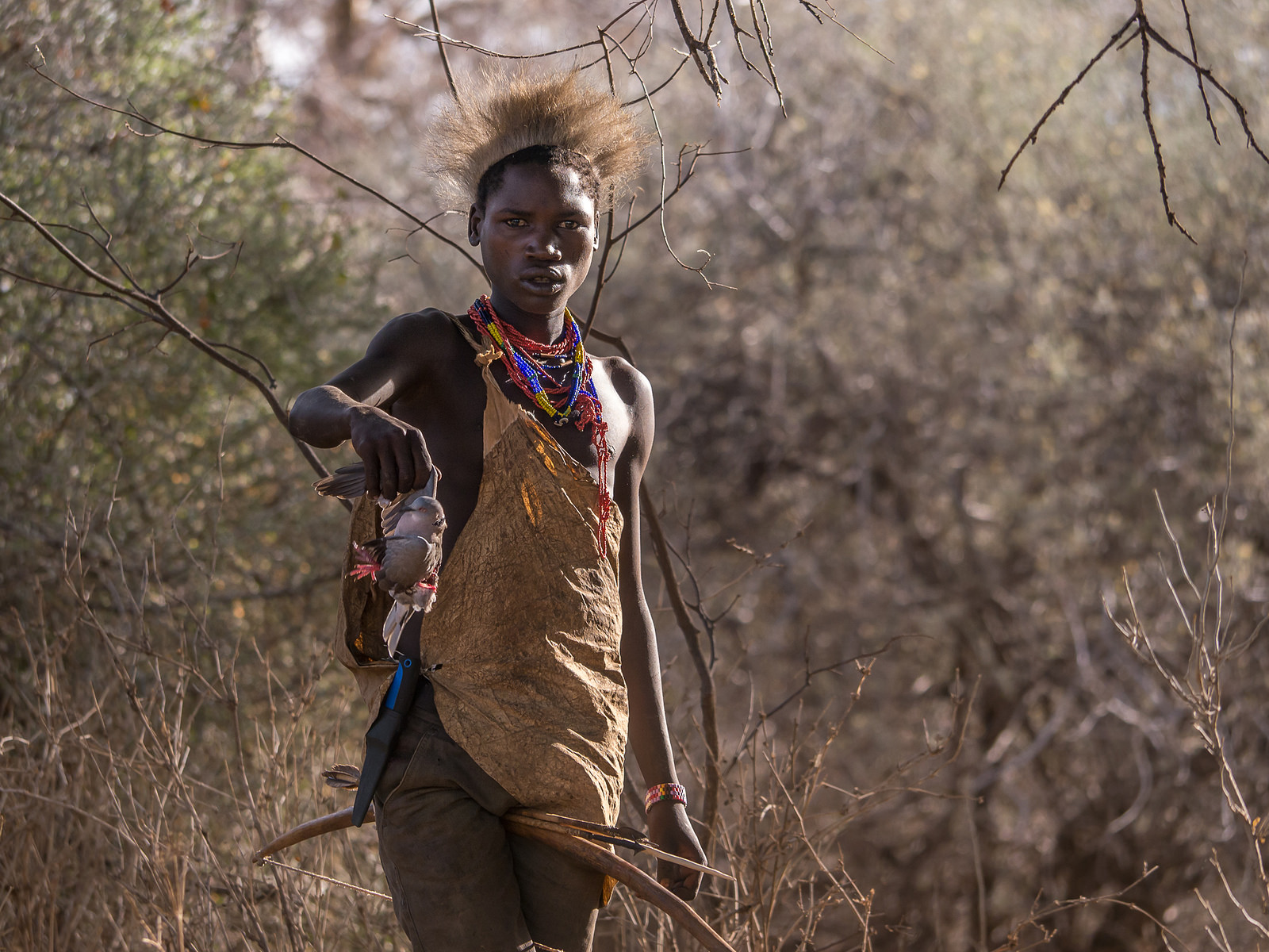 A young African hunter holds up the bird he has successfully caught. Hadzabe tribe, near Lake Eyasi, Tanzania