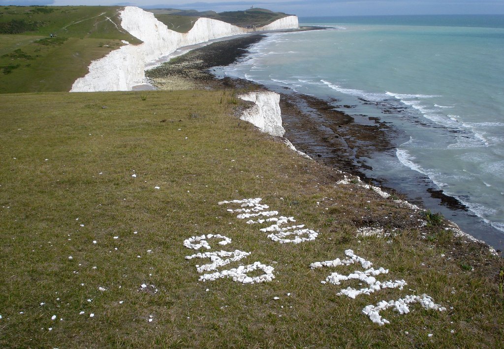 The words Mind The Gap are written in white stones on the edge of iconic English cliffs facing France