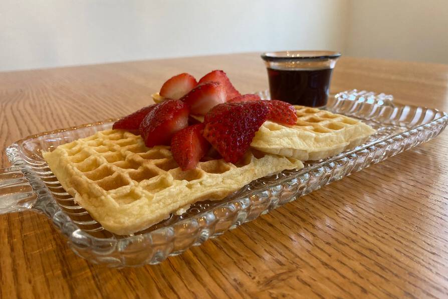 [photo: a glass tray with two waffles topped with pieces of strawberry and a glass of maple syrup]