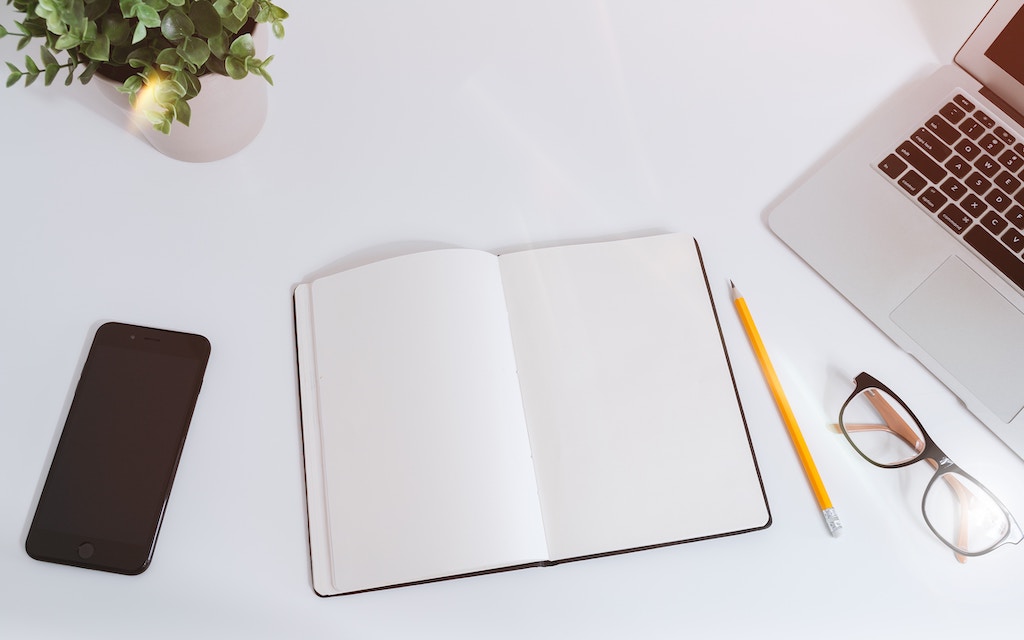 smart phone, open book with empty page, laptop, pencil and eye glasses on a table