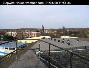 Sopwith house weather cam. Taken on the 21/04/10 at 11:51 and 34 seconds. 
In the foreground are the safety rails on the flat part of the roof. Nearby ther are low rise industrial buildings, beyond those are block of flats. 
In the distance there's a church steeple.