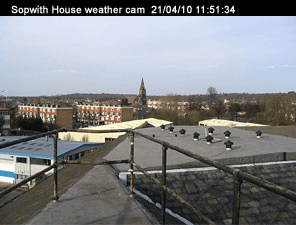 Sopwith house weather cam. Taken on the 21/04/10 at 11:51 and 34 seconds. In the foreground are the safety
  rails on the flat part of the roof. Nearby ther are low rise industrial buildings, beyond those are block of flats. In the distance there's a
  church steeple.