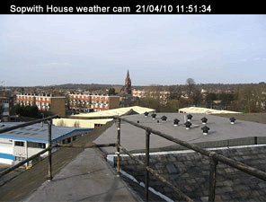 Sopwith house weather cam. Taken on the 21/04/10 at 11:51 and 34 seconds. In the foreground are the safety rails on the flat part of the roof. Nearby ther are low rize industrial buildings, beyond those are block of flats. In the distance there’s a church steeple.