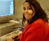 woman wearing casual clothing and smiling, sitting in front of computer