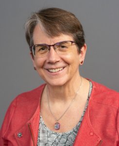 Judy Brewer: a woman with dark hair, glasses, wearing a necklace and coral top 