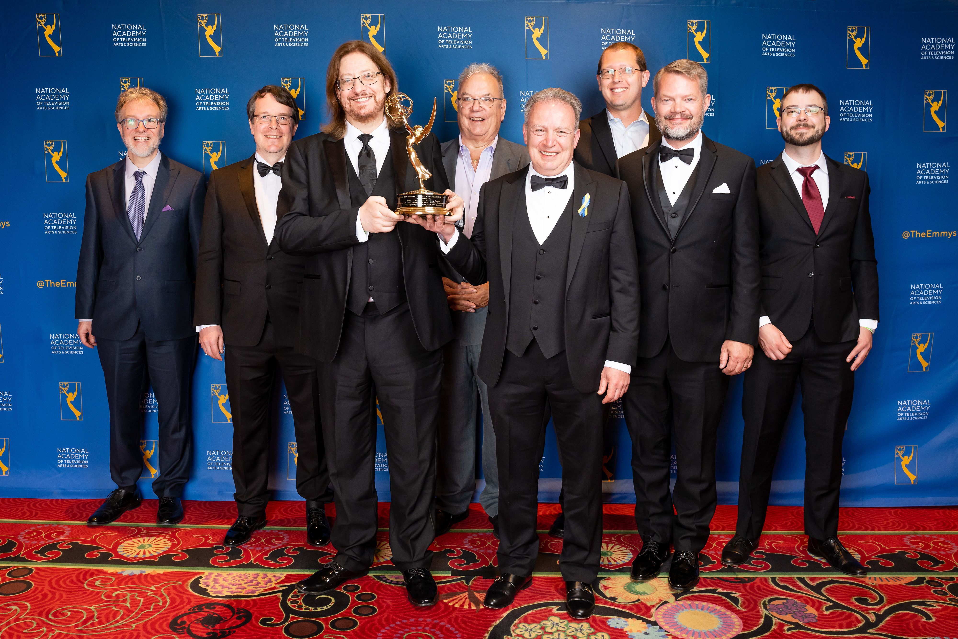 men in suits from the WOFF Working group, one holding an Emmy