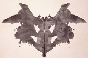 An abstract, freeform vertically symmetrical black inkblot on a light background.